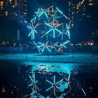 The Neonagon, Darling Harbour, with a polygon with neon tube edges moving on rotors reflected blue in the puddles below