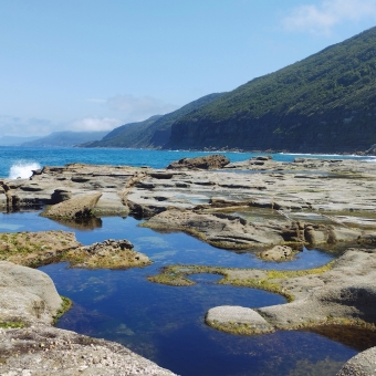 Royal National Park, Lilyvale, with the rockpool reflecting the bluest sky, with the rocks leading to the ocean which then leads to the coast in the distance which rises into a green mountain