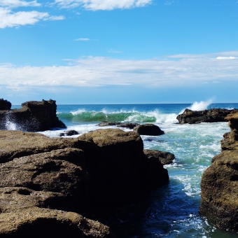 Rocky Outlook, Caves Beach, with many rocks protruding from rough ocean waves below the bluest sky