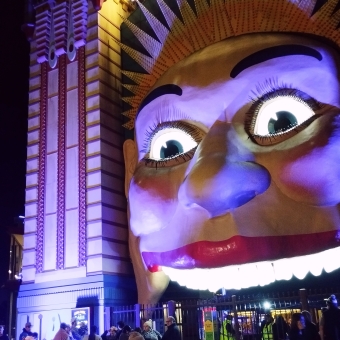 The Well-Lit Face, with the entrance to Luna Park lit up from behind as though the face's eyes and teeth are glowing, with purple and red lights casting eerie shadows across it
