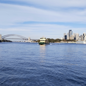 Ferry Far Away, Birchgrove Wharf, Birchgrove, with a ferry some distance away over water in centre frame, with the Sydney Harbour Bridge and northern CBD in the distance almost against the horizon