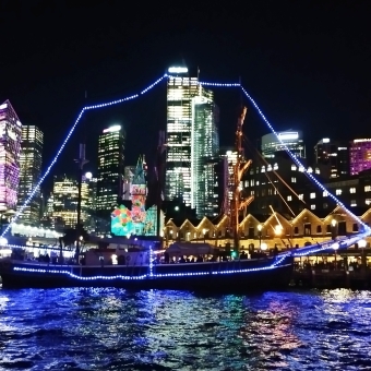 Ship's Outline, Dawes Point, with an old sailing ship traced with blue light and city building lit up behind