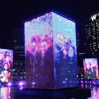 Projected Families, Darling Harbour, with three large LED screens positioned like mini-skyscrapers sitting in the water which are projecting a different group of people of each face