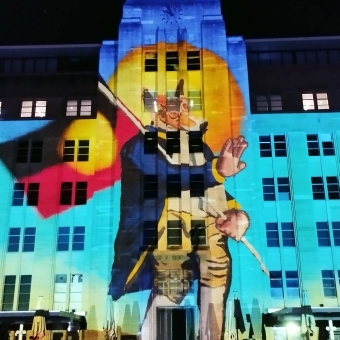King Dingo, Museum of Contemporary Art, with a projection of an anthropomorphic dingo wearing a colonel's outfit carrying an Aboriginal flag over his shoulder