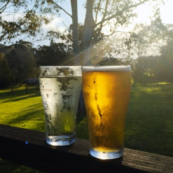 Share A Schooner, Wollombi Tavern, Wollombi, with two pub glasses sitting on a railing in the foreground, with a gum tree and a streak of afternoon sunlight
