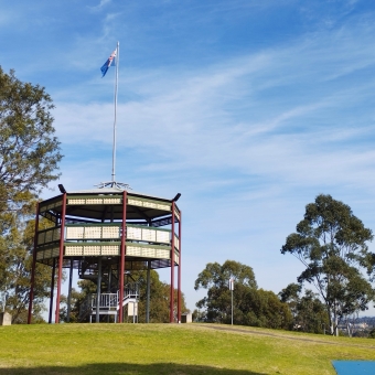 Observe The Observatory, Peace Park, Ashbury, with a two-storey octagonal wooden structure which has a viewing platform atop it, with blue sky and wispy coulds behind it and the occasional tree to its sides