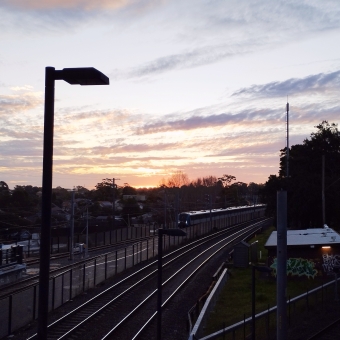 The Sun Sets On The Metro Test, Dulwich Hill Station, Dulwich Hill, with a testing metro train on the tracks below, with a glowing orange sunset streaking through clouds above