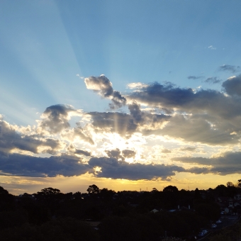Radiating Sunset, Dulwich Hill, with a yellow sun streaming out from behind clouds with distinct blues and oranges