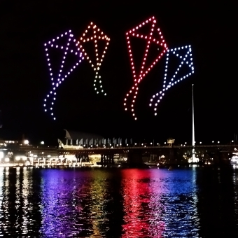 Working Through The Evening, from Sydney Harbour Bridge, with some of the skyscrapers of Circular Quay and cranes surrounding them which are all in front of sunset colours
