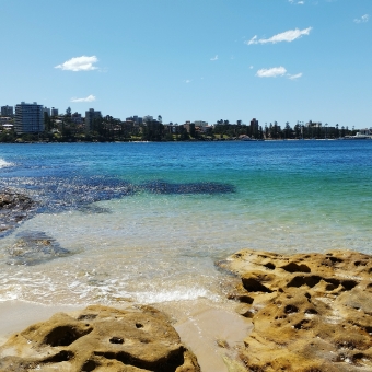 The Spit to Manly Walk, Delwood Beach, Manly, with shallow water and rocks in front and cost in the distance