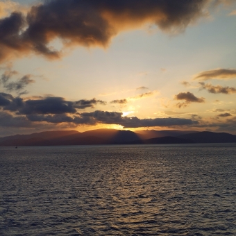 Sunset Over Water, Shute Harbour, with an orange sunset behind silhouetted clouds and mountains