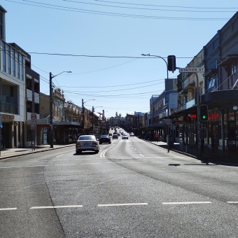 Grey Main Road, Enmore Road, Newtown, with a older street full of empty shop fronts, powerlines, and cars