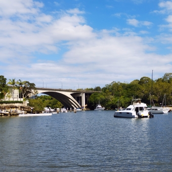 Blissful Waters, Tarban Bay, Hunters Hill, with an arch bridge which connects two green headlands over rippling bay water and some small water vessels