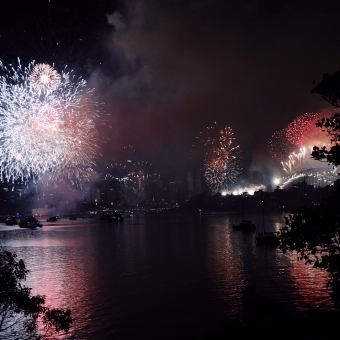 Starting New Years With A Bang, Cremorne Point, with white and red fireworks coming up from Fort Denison on the left and out from the Sydney Harbour Bridge to the right